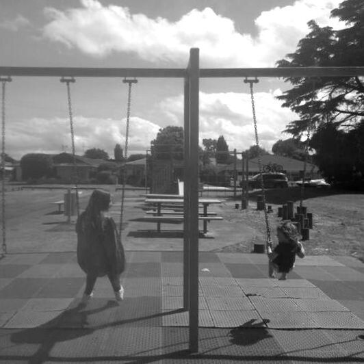 Picture of two children swinging on a swing each.  They are looking towards each other smiling.