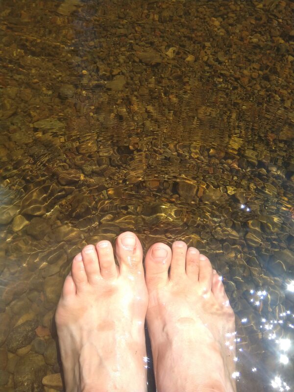 A woman's feet sitting in a stream bed with water flowing over them.
