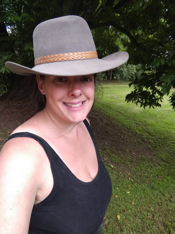 Selfie of a woman wearing a black tank top and a grey cowboy hat. The woman is smiling.