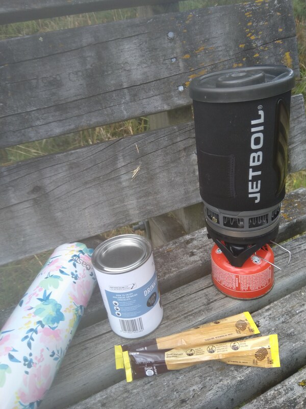 Picture of a Jet Boil portable stove with nestle latte sachets, hot chocolate powder and a drink bottle of water