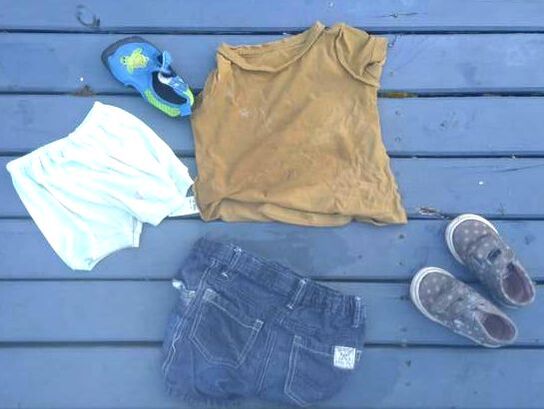 Picture of a small child's clothing laid out on painted timber decking. the clothing is wet. There are two pairs of shorts, a tshirt and one pair of shoes plus another single right shoe.